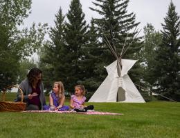 A family picnicking outdoors in front of a teepee.